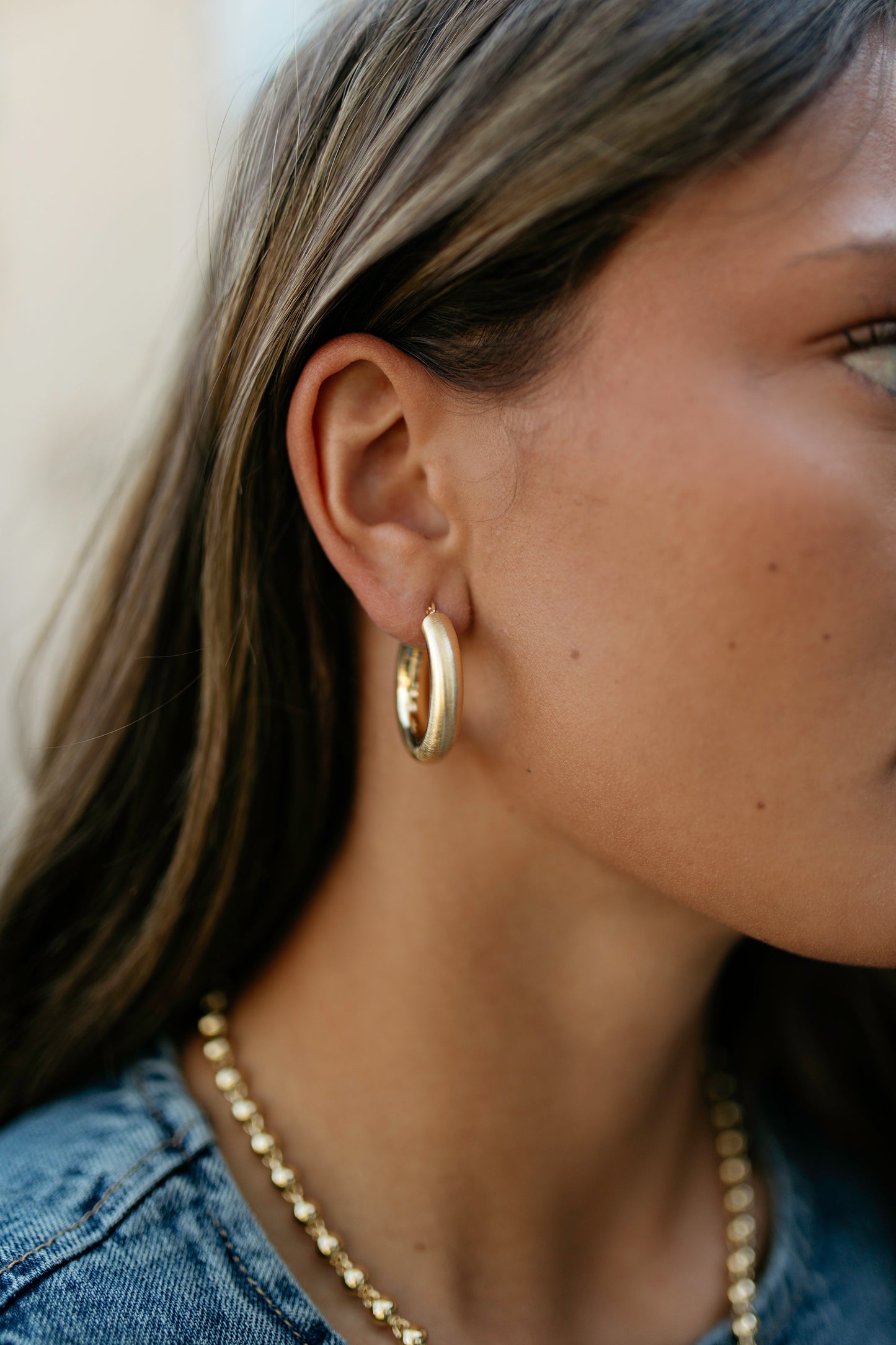 Close-up of a person wearing gold hoop earrings and a necklace.