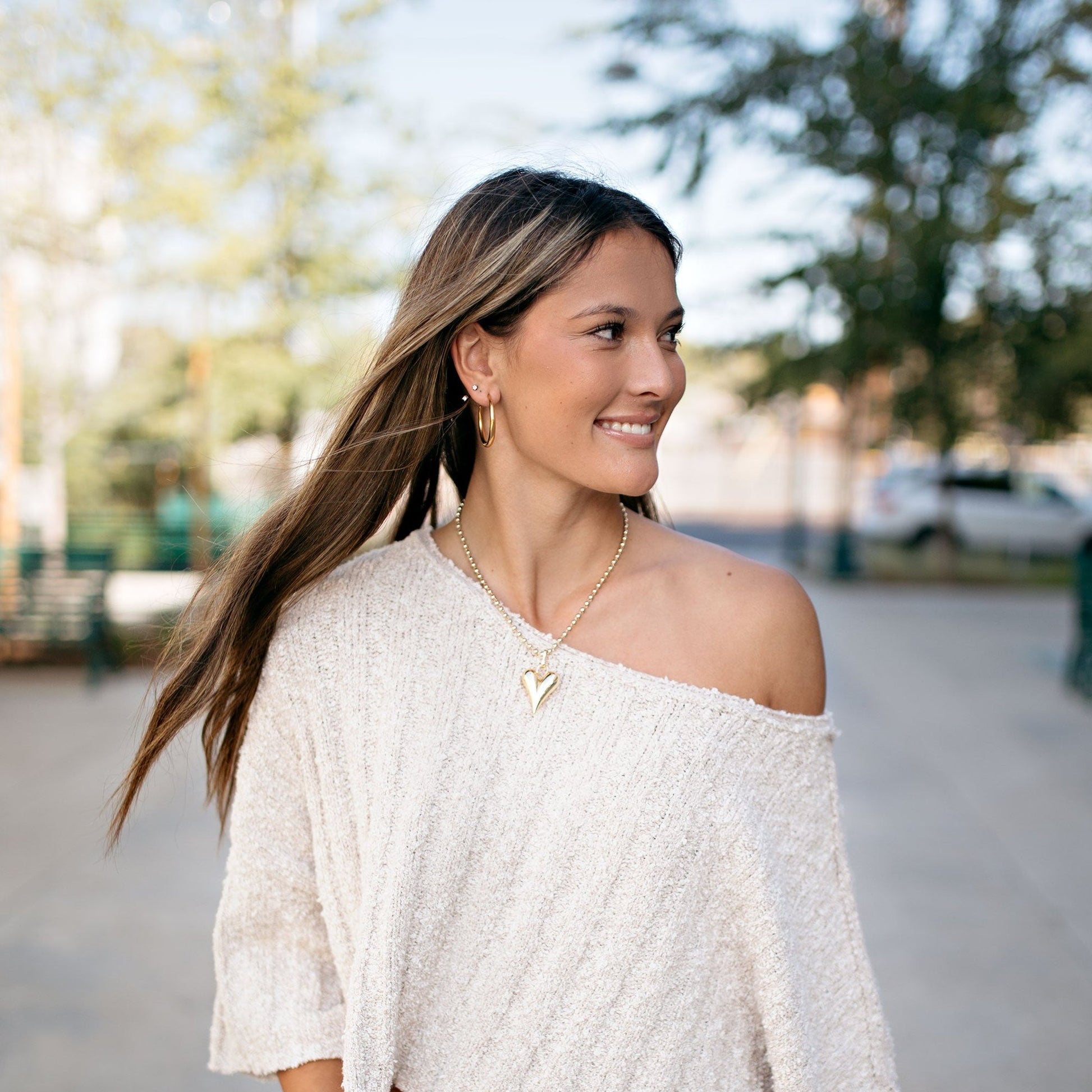 Gold Hoop Earrings with heart charm necklace. with a white knit top in downtown