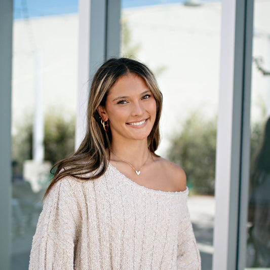 Girl in cream sweater with gold hoop earrings and gold and white charm necklace